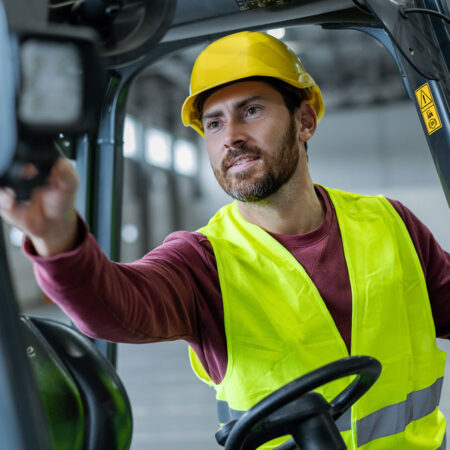 Gabelstaplerfahrer-Warnweste Ein Gabelstaplerfahrer mit Warnweste und Schutzhelm richtet seinen Gabelstapler ein.